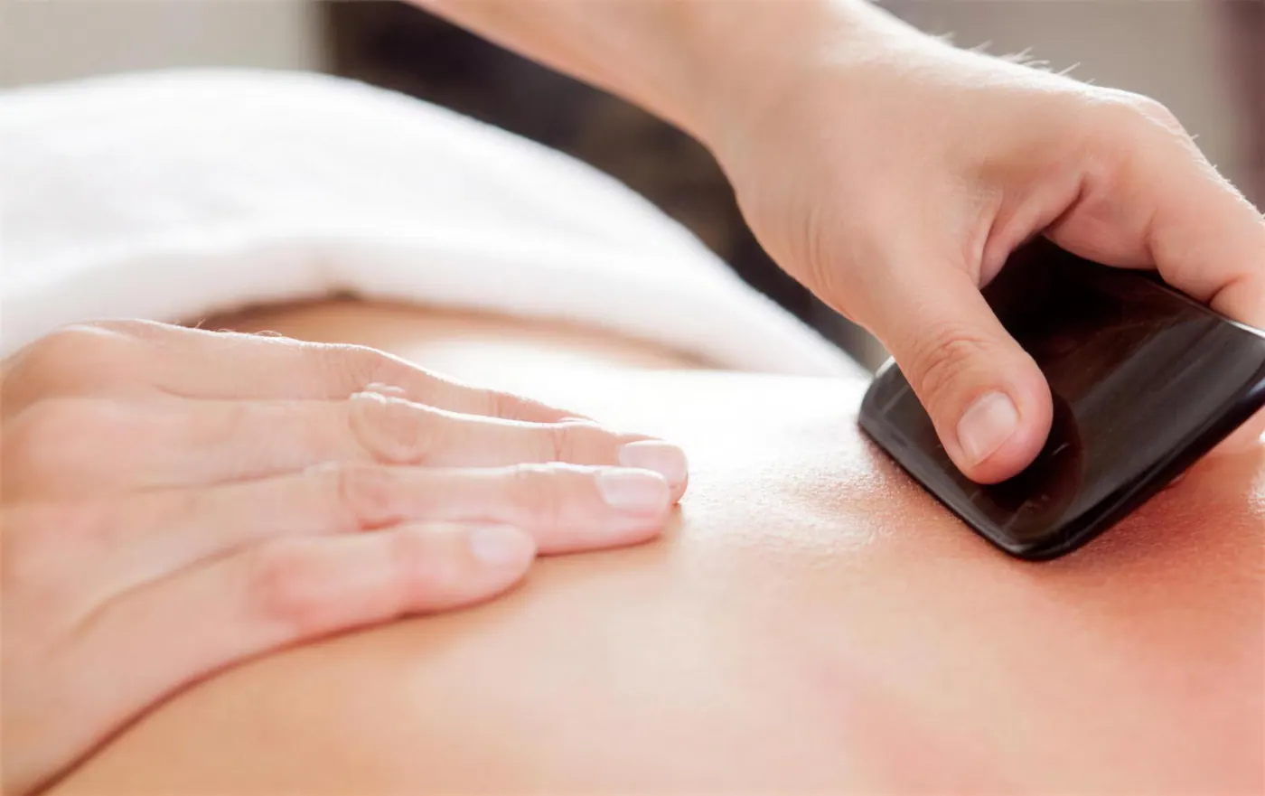 A dark natural-stone Gua Sha tool gliding across a client's back.